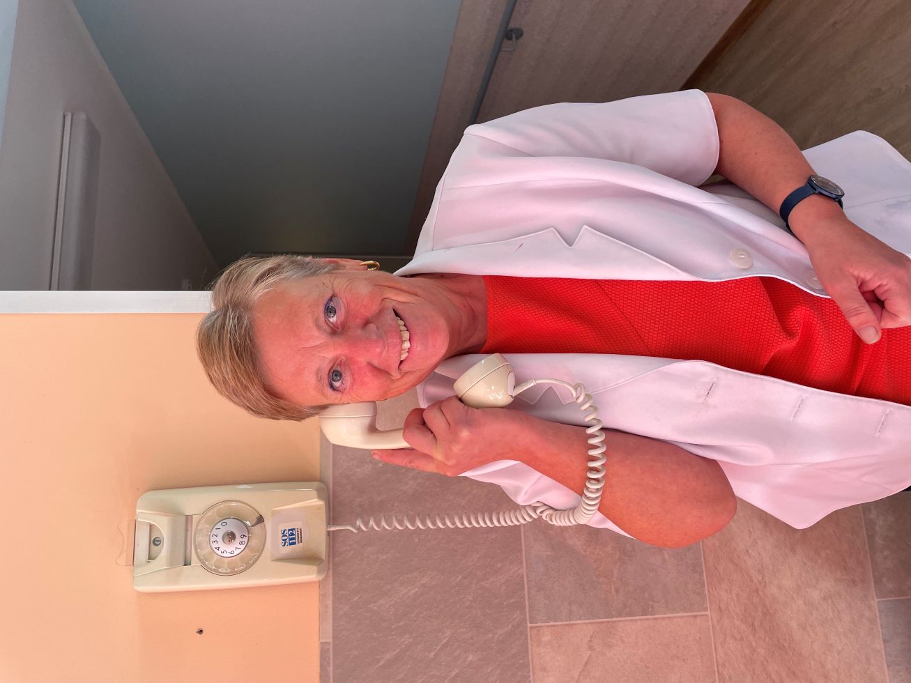 Anne-Ly Reede poseerimas kettaga telefoniga, mis on hooldekodu seinal aksessuaarina ja tuletab mäluhäiretega inimestele meelde kauneid möödunud aegu.